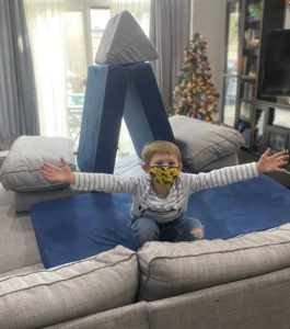 Child proudly shows off a pillow fort he created with the cushions of the couch.